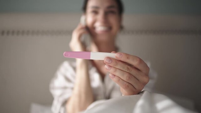 A happy woman holding a pregnancy test while talking on her mobile phone. Concept joyful experience of sharing important news.