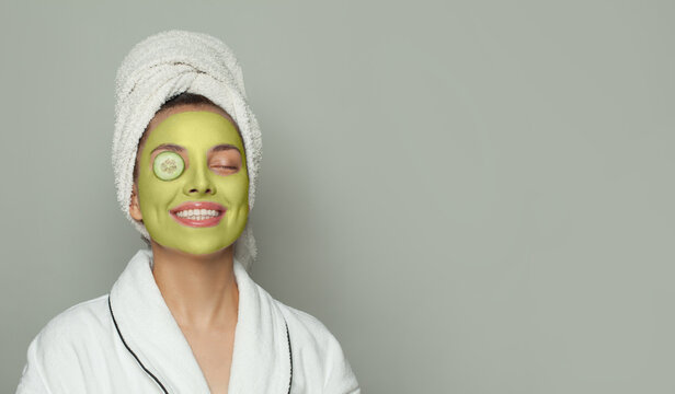Portrait of young woman in green organic cosmetic face mask holding cucumber slices