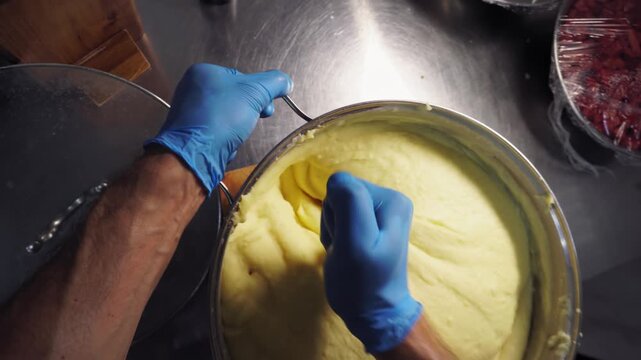 A man by his hands in the kitchen stirs mashed potatoes in a saucepan