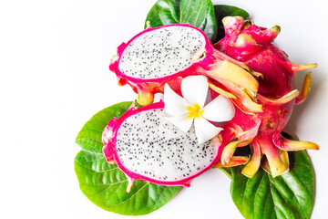 Pitahaya dragon fruits - whole and a half - with frangipani flower and green leaves on white table....