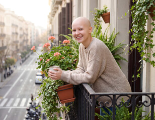 Obraz premium Happy woman with shaved head holding coffee cup and standing in a balcony showing positivity