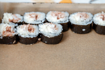Row of maki sushi with tuna and rice in a takeaway box on a table