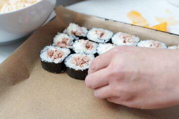 Crafting homemade sushi rolls filled with delicious tuna and rice on a brown baking sheet, showing culinary creativity in the kitchen