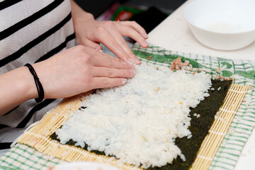 Making sushi at home; rice is spread on the nori seaweed, using hands over a bamboo rolling mat