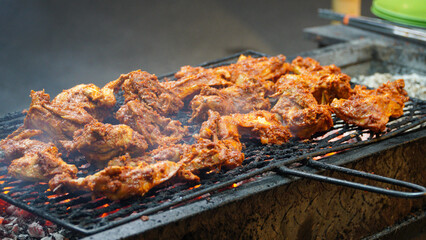 Spicy grilled chicken being grilled using a manual charcoal burner, the smoke of which can be seen in the air at night.