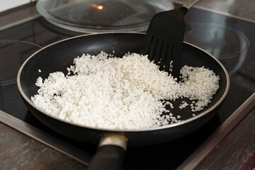 Rice dances in the pan under the watch of a black spatula on a modern electric stove