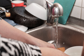 Washing up after a meal at home shows a collection of dirty dishes stacked around the sink, and running water