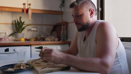 Man in kitchen cleaning and eating dried fish