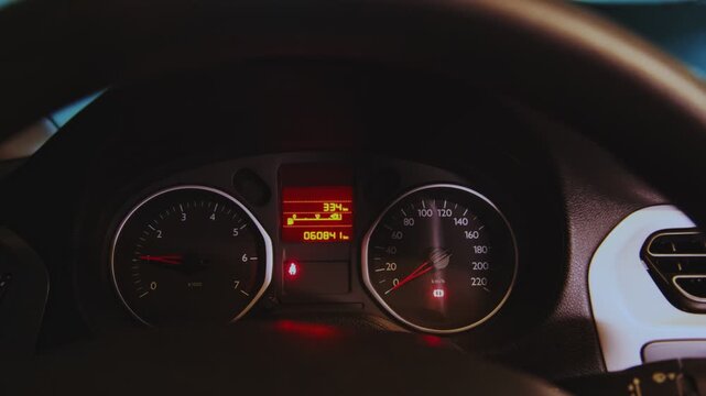 Car's dashboard with the tachometer needle rising as the engine starts and warning lights illuminating