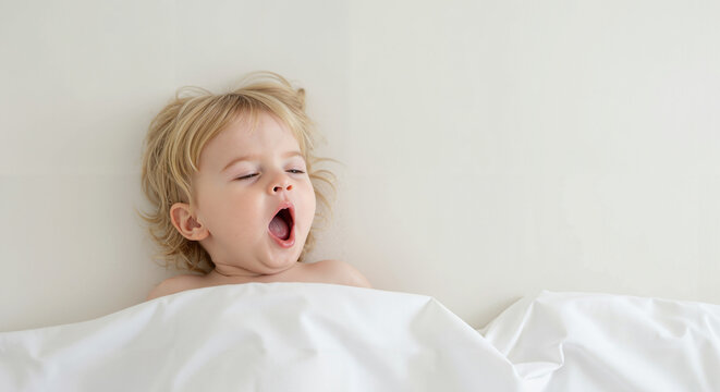 Baby yawning while lying in bed with white bedding - Powered by Adobe