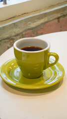 a glass of hot americano in a green glass cup placed on the edge of a wooden table