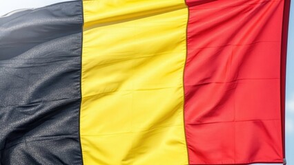 Obraz premium Vibrant national flag with black, yellow, and red stripes proudly waving in the wind, symbolizing national identity and heritage in the sunlight