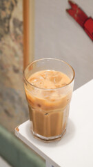 a glass of iced coffee with milk in a clear glass placed on the edge of a wooden table
