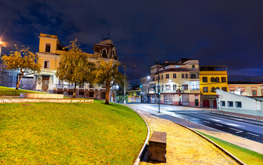 Plaza Garcia Moreno sits near Basilica del Voto Nacional in Quito, Ecuador. Green park features stone benches and views of colorful colonial buildings in historic center