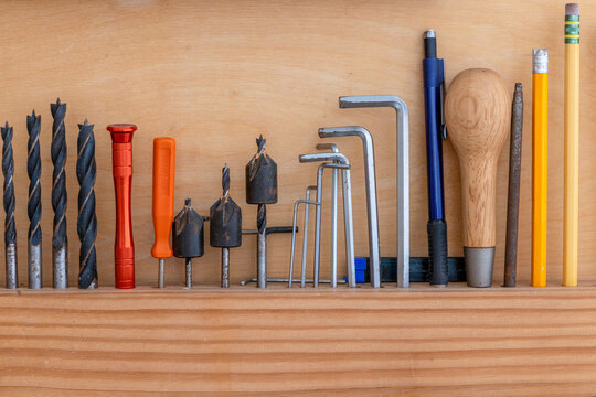 Various hand tools and drill bits are neatly arranged on a wooden shelf. The tools include different sizes of drill bits, wrenches, and writing instruments, ready for use in crafting.