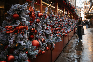Christmans decorations adorn the streets as a person walks through a festive market on a rainy day.