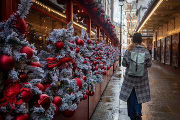 Christmans decorations adorn the streets as a person walks through a festive market on a rainy day.