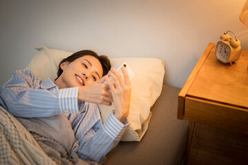 ベッドに横になり、スマートフォンを操作している女性