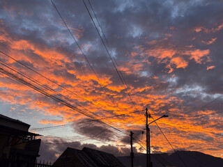 Stunning fiery sunset with dramatic clouds over rooftops and distant mountains view