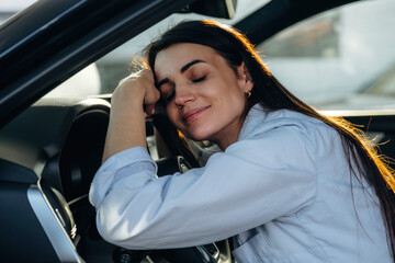 Resting, leaning on the steering wheel. Woman is sitting in the modern car, happy new owner