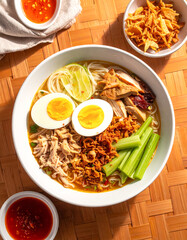 Soto mie with yellow noodles and soft-boiled egg in vibrant overhead style on bamboo mat