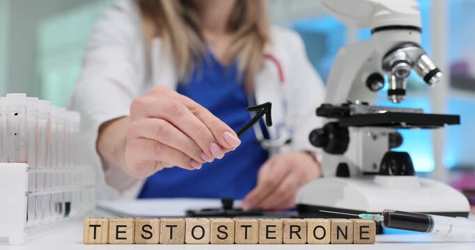 Wooden blocks spell word Testosterone near microscope standing on table. Laboratory scientist raises male symbol studying testosterone effect on body