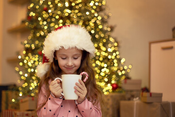 Portrait of a little girl with a mug in her hands on Christmas Eve against the background of a...