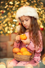 Little girl with oranges near the New Year tree, Christmas cozy mood, Christmas Eve background
