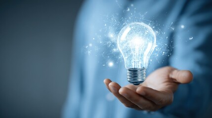 A bright lit lightbulb with rays floating above an outstretched hand against a bluish backdrop,