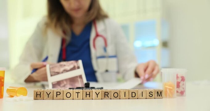 Wooden blocks spell word Hypothyroidism by thyroid scan images. Endocrinology doctor checks report planning therapy for hypothyroidism at appointment