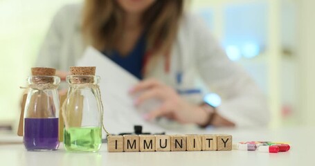 Wooden blocks spell word Immunity near purple and green liquids in flasks. Immunology specialist reviews lab data evaluating patient immune status - Powered by Adobe