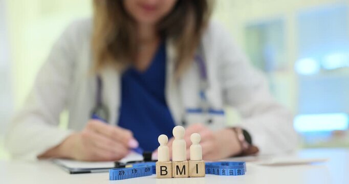 Wooden blocks spell BMI standing under wooden people figures and rolled blue tape. Nutrition doctor writes numbers calculating BMI value for patient
