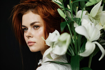 Fototapeta premium A serene young woman with red hair, surrounded by white lilies, exudes a natural elegance and calm, perfect for themes of beauty and emotional connection