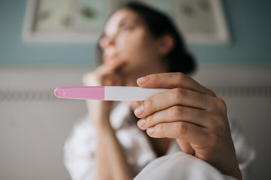 Woman holding a pregnancy test with a thoughtful expression, sitting in a cozy room, surrounded by soft lighting and calming decor, reflecting on potential life changes