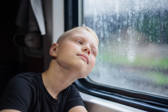 Dreamy child portrait by a rainy train window for emotional storytelling, real authentic photo.