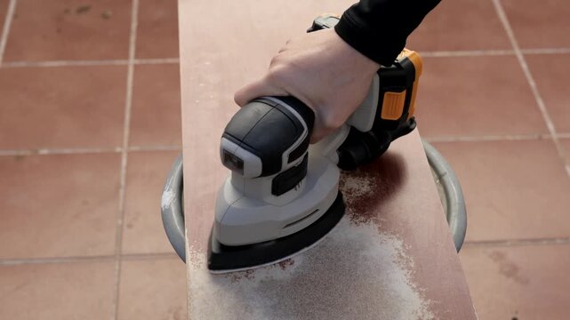 Hand sanding wood surface with battery-powered sander reducing rough patches