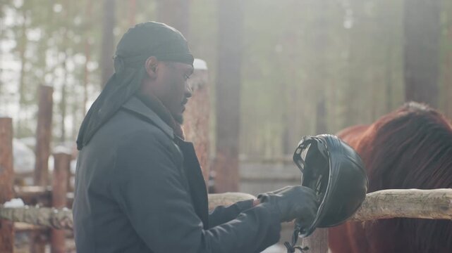equestrian ritual preparation, individual in stable adjusting gear before riding session begins, horse rider meticulously prepares helmet and gloves prior to starting ride in wooded stable