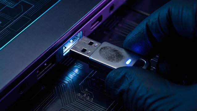 Gloved hand inserting biometric USB hardware security key with fingerprint into laptop port, cybersecurity concept