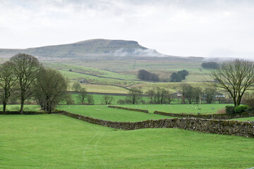 Pen-Y-Ghent with atmospheric clouds and Yorkshire Dales farmland. This iconic hill forms one part of the Yorkshire three peaks challenge.