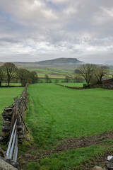 Pen-Y-Ghent with atmospheric clouds and Yorkshire Dales farmland. This iconic hill forms one part of the Yorkshire three peaks challenge.