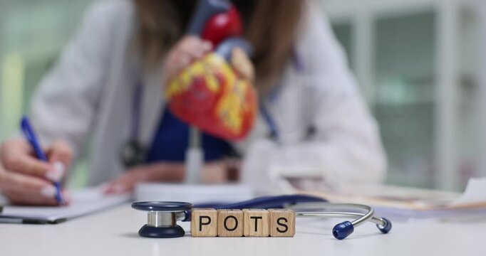 Wooden blocks spell term POTS near heart model and stethoscope. Woman doctor records heart rate with blood pressure data explaining POTS syndrome