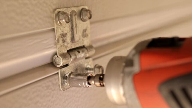 Close-up of impact driver tightening final screw on garage door hinge