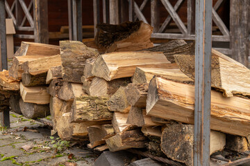 Chopped firewood lies stacked next to a wooden shelter, prepared for winter use in a calm outdoor setting with rustic charm