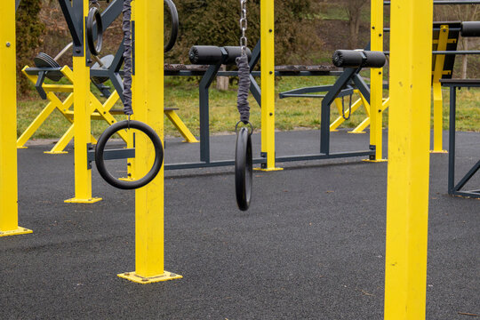 Bright yellow workout equipment stands in a fitness area, showcasing gym rings ready for various exercises in a grassy park setting