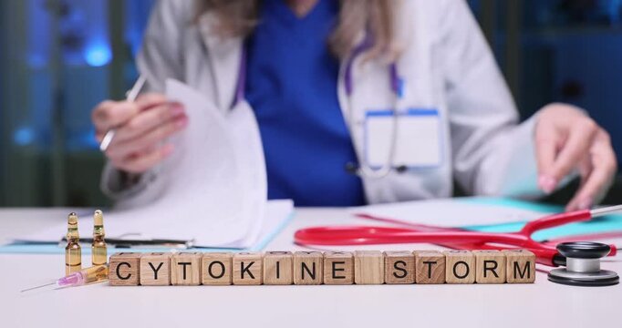 Wooden blocks spell phrase Cytokine Storm on hospital desk. Medical woman sorts patient papers evaluating serious cytokine storm risk slow motion