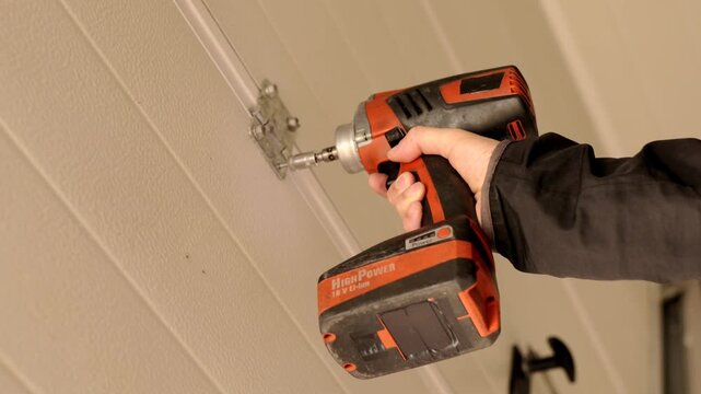 Impact driver mounting garage door hinge onto metal panel