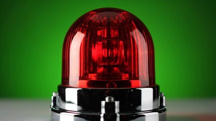 Close-up of a red emergency light, a beacon of warning, against a vibrant green backdrop.