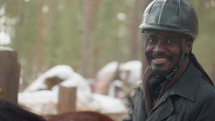 cheerful rider wearing protective headgear interacts calmly with horse amidst winter landscape, content man with helmet shares relaxed moment with his horse in snowy paddock setting