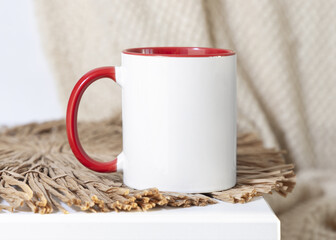 White accented coffee mug with red handle on beige placemat Close up. Boho mock up