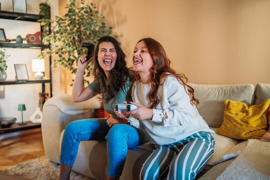Cheerful women friends playing video games on sofa